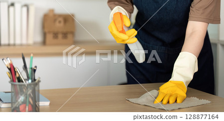 Home Cleaning. Woman cleaning desk with yellow rubber gloves. 128877164