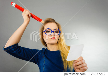 Confused woman holds big pencil note paper in hand Confused woman holds big pencil note paper in hand 128877212