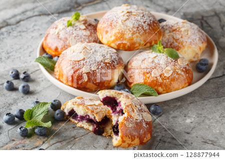 Homemade French brioche buns with blueberries and almond petals close-up in a plate. Horizontal 128877944