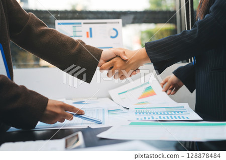 Business people shaking hands in office. Two business partners shaking hands after signing a contract in office. Business people shaking hands in office. Two business partners shaking hands after signing a contract in office. 128878484