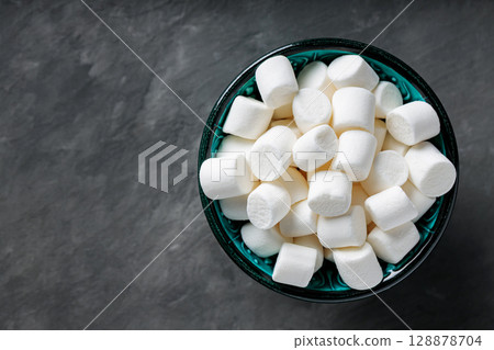 White Marshmallow Candies in Bowl on Dark Gray Background Top View Copy Space 128878704