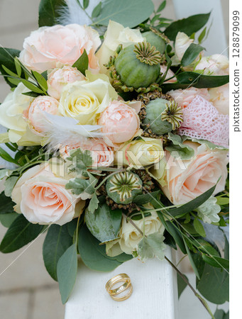 Close-up of a pastel wedding bouquet with roses, poppy pods, and two golden rings, symbolizing love and marriage. Close-up of a pastel wedding bouquet with roses, poppy pods, and two golden rings, symbolizing love and marriage. 128879099