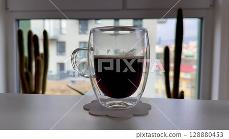 A delightful cup of coffee in a stylish glass, set against a vibrant urban backdrop 128880453