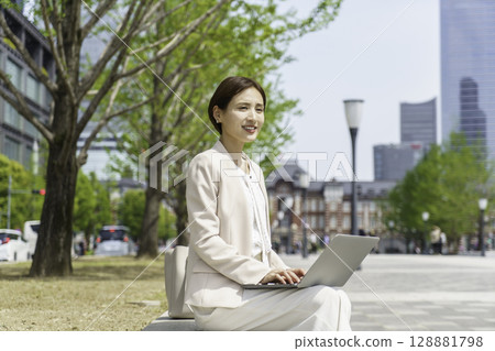 一位年輕的女商人坐在長椅上用電腦 128881798