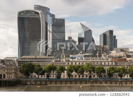 the City of London from across the River Thames, featuring prominent modern skyscrapers rising prominently behind older, more traditional buildings along the River Thames. 128882041