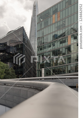 The sleek stainless steel handrail gracefully curves in the foreground, leading the eye towards the imposing modern buildings. The sleek stainless steel handrail gracefully curves in the foreground, leading the eye towards the imposing modern buildings. 128882052