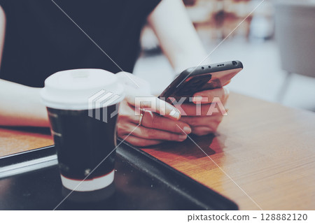 Woman's hands looking at her smartphone in a cafe Woman's hands looking at her smartphone in a cafe 128882120