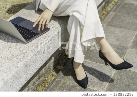 Close-up of the feet of a young businesswoman sitting on a bench and using a laptop Close-up of the feet of a young businesswoman sitting on a bench and using a laptop 128882292