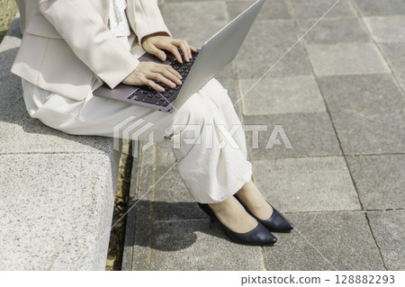 Close-up of the feet of a young businesswoman sitting on a bench and using a laptop Close-up of the feet of a young businesswoman sitting on a bench and using a laptop 128882293