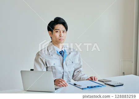 A young man in work clothes doing office work 128883259
