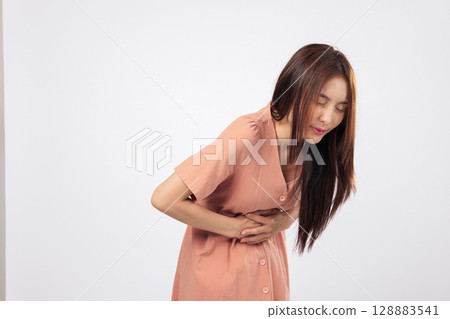 Stomach pain and stomach tension seen in a young Asian woman with hand on belly suffering from female health condition isolated on studio white background Stomach pain and stomach tension seen in a young Asian woman with hand on belly suffering from female health condition isolated on studio white background 128883541