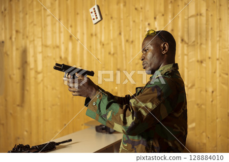 Man aiming pistol at shooting gallery, participating in elite level marksmanship training program, testing precision. Army unit at firing range doing intensive shooting course with gun Man aiming pistol at shooting gallery, participating in elite level marksmanship training program, testing precision. Army unit at firing range doing intensive shooting course with gun 128884010