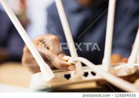 African american woman restarting their WI FI modem with the LAN cable, struggling to solve their internet connectivity issues and signal loss. Unstable wireless network for freelancing. Close up. 128884038