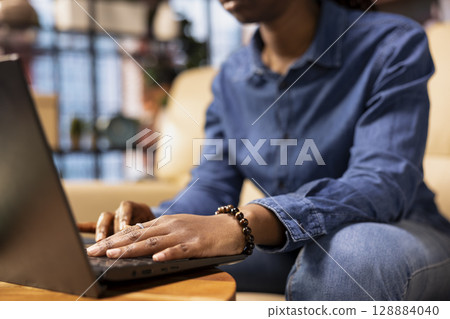 Person at home browsing internet on laptop and researching information online, accessing websites and reading articles while she sits on the couch. Find data relevant to work tasks. 128884040