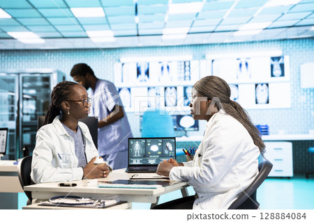 Female general practitioner examining medical data with a patient, fostering interaction and trust during expert consultation focused on wellness. African american girl asks for advice. Female general practitioner examining medical data with a patient, fostering interaction and trust during expert consultation focused on wellness. African american girl asks for advice. 128884084