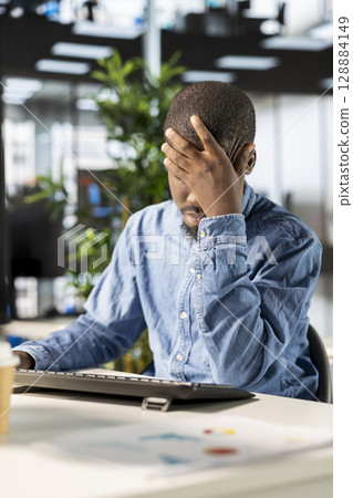 Stressed general manager working under pressure on crucial organizational tasks, dealing with burnout and mental exhaustion. African american man getting overwhelmed by project deadlines. Stressed general manager working under pressure on crucial organizational tasks, dealing with burnout and mental exhaustion. African american man getting overwhelmed by project deadlines. 128884149