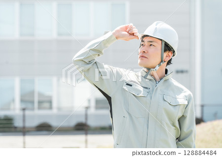 Asian male worker wearing work clothes and a helmet Asian male worker wearing work clothes and a helmet 128884484