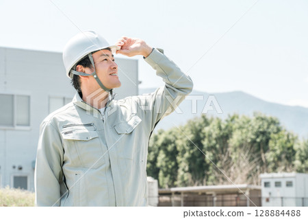 Asian male worker wearing work clothes and a helmet Asian male worker wearing work clothes and a helmet 128884488