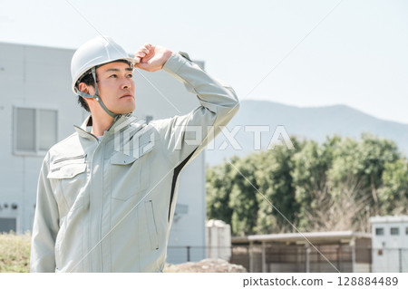 Asian male worker wearing work clothes and a helmet Asian male worker wearing work clothes and a helmet 128884489