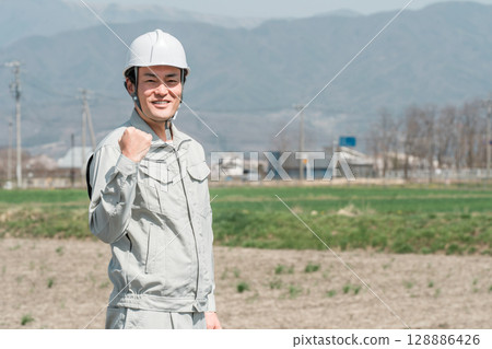 身穿工作服、頭戴安全帽的亞洲男工人揮拳擺姿勢（遷徙、鄉村、 I 型轉彎） 128886426