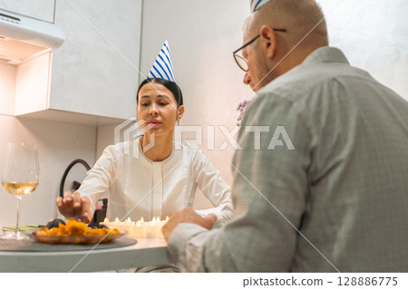 Birthday Couple Kitchen Celebration: Woman presents birthday cake candles to man during intimate home birthday party. Birthday Couple Kitchen Celebration: Woman presents birthday cake candles to man during intimate home birthday party. 128886775