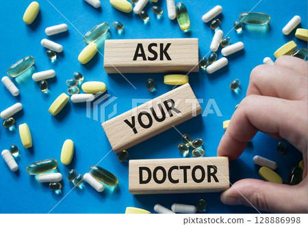 Ask Your Doctor symbol. Concept word Ask Your Doctor on wooden blocks. Doctor Hand. Beautiful blue background with pills. Medicine and Ask Your Doctor concept. Copy space 128886998