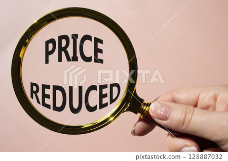 Price reduced symbol. Magnifying Glass with Concept word Price reduced. Beautiful pink background. Businessman hand. Business and Price reduced concept. Copy space 128887032