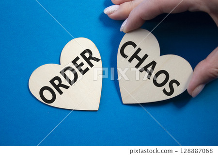 Chaos or Order symbol. Concept word Chaos or Order on wooden hearts. Businessman hand. Beautiful blue background. Business and Chaos or Order concept. Copy space 128887068