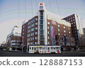 [Logo driver sign blurred] Hakodate City Tram 800 series going around the curve in front of Hakodate Station 128887153
