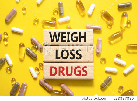 Medicine symbol. Concept words Weight Loss Drugs on wooden blocks. Beautiful yellow background with pills. Medicine concept and Weight Loss Drugs. Copy space 128887880