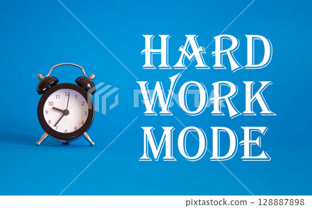 Hard Work Mode symbol. Concept word Hard Work Mode on Beautiful blue background with alarm clock. Business and Hard Work Mode concept. Copy space Hard Work Mode symbol. Concept word Hard Work Mode on Beautiful blue background with alarm clock. Business and Hard Work Mode concept. Copy space 128887898
