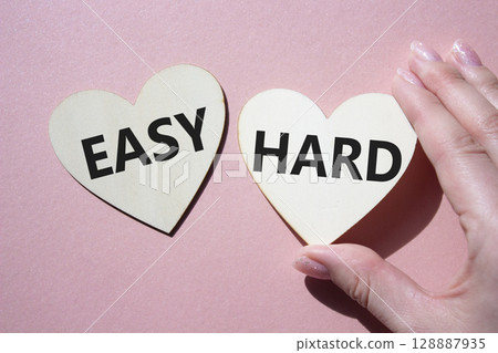 Easy or Hard symbol. Concept word Easy or Hard on wooden hearts. Businessman hand. Beautiful pink background. Business and Easy or Hard concept. Copy space 128887935