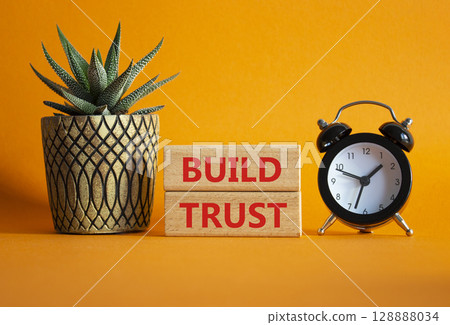 Build trust symbol. Wooden blocks with words Build trust. Beautiful orange background with alarm clock and succulent plant. Business and Build trust concept. Copy space. 128888034