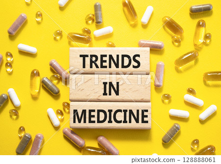 Medicine symbol. Concept words Trends in Medicine on wooden blocks. Beautiful yellow background with pills. Medicine concept and Trends in Medicine. Copy space Medicine symbol. Concept words Trends in Medicine on wooden blocks. Beautiful yellow background with pills. Medicine concept and Trends in Medicine. Copy space 128888061