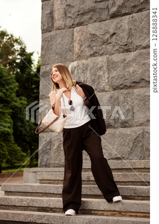 Smiling young woman joyfully descending outdoor stone staircase. 128888341