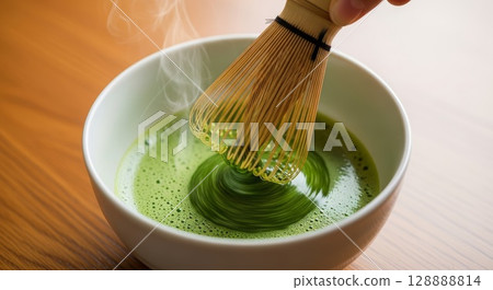 Traditional bamboo whisk whisking vibrant green matcha tea powder creating foam in white ceramic bowl on wooden surface 128888814