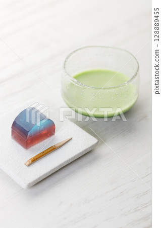 Cup of fresh matcha tea, green tea and Kingyoku can, traditional Japanese jelly confectionery on white wooden table. 128889455