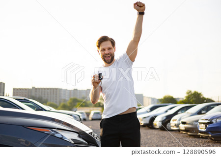 A happy man celebrates buying a new car, holding the keys up in victory at the dealership. A happy man celebrates buying a new car, holding the keys up in victory at the dealership. 128890596