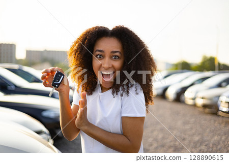 A joyous woman beams with excitement, proudly displaying her new car keys at a dealership, signifying a successful purchase. 128890615