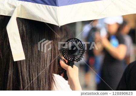 Woman walking with a handheld fan Portable fan 128890623