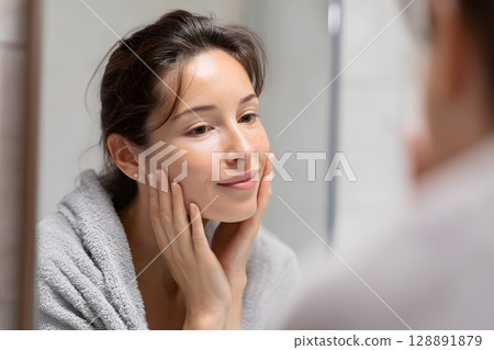 Woman checking facial results in small mirror 128891879