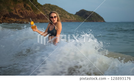 Woman stand knee-deep in sea on sunset. Girl on beach in green s 128893176