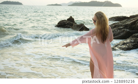 Woman stand on a reef rock stone in sea on sunset. Girl on beach 128893216