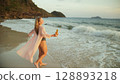 Woman walks on sunset on beach against background of sea. Girl i Woman walks on sunset on beach against background of sea. Girl i 128893218