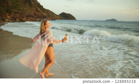 Woman walks on sunset on beach against background of sea. Girl i Woman walks on sunset on beach against background of sea. Girl i 128893218