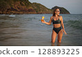 Woman stand knee-deep in sea on sunset. Girl on beach in green s Woman stand knee-deep in sea on sunset. Girl on beach in green s 128893225