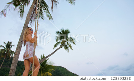 Sexual woman spends her vacation at the seaside. The girl is swinging on a swing. Sexual woman spends her vacation at the seaside. The girl is swinging on a swing. 128893228