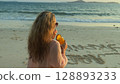 Woman walks on sunset on beach against background of sea. Girl i Woman walks on sunset on beach against background of sea. Girl i 128893233