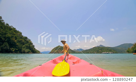Man with sunglasses and hat rows pink plastic canoe along sea ag Man with sunglasses and hat rows pink plastic canoe along sea ag 128893247