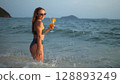 Woman stand knee-deep in sea on sunset. Girl on beach in green s Woman stand knee-deep in sea on sunset. Girl on beach in green s 128893249